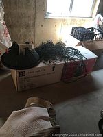 Black plastic tree stand, a long green wire string of lights, sitting on top of sealed box labeled '7.5FT Sierra Nevada Tree - Dual LED'. Box description and weight visible.