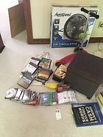 Photo showing storage ottoman, assorted CDs, DVDs, VHS tapes, Aerogear Air Circulator box, and Mini Kickboard scooter.