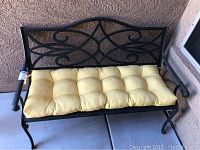 Full front view of the black metal outdoor bench with yellow tufted cushion.