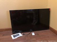 Front view of the 40 inch Vizio TV on the floor, showing the screen, power cord, and user manual nearby.