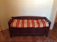 Front view of dark wood bench with striped cushion on seat and low back with vertical slats.