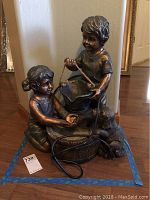 Front view of bronze finish fountain sculpture showing two children and dog with power cord wrapped around base.
