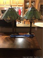 Two Tiffany style lamps with green stained glass shades on a wooden table