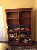 Full front view of warm toned wooden bookcase filled with various kitchenware items to show shelving and size.
