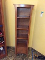 Front view of the tall warm-toned wood shelving unit showing the overall structure including shelves and drawer.