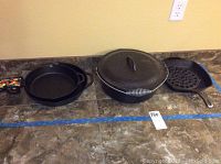 Three cast iron cookware pieces on counter: small skillet with colorful fabric handle cover, large skillet, and Dutch oven with lid and coiled handle.
