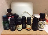 Photo showing diffuser and 9 assorted essential oil bottles with labels visible, placed on a wooden surface.