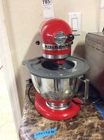 Front view of the red KitchenAid mixer on a marble countertop showing the stainless steel mixing bowl attached.
