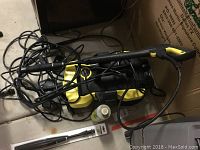 Photo showing Karcher power washer main unit with attached cords and spray gun, also a small bottle of cleaning fluid present.