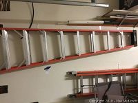 Red and silver Werner extension ladder, approximately 24 feet long, hung on a wall with black end caps visible