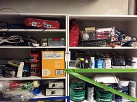 Shelves containing assorted hardware items including nails, screws in containers, power strips, paint supplies, and boxes of outlet covers.