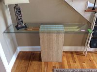 Front view of the side table showing the full glass top and marble/stone base against the wall, with a lamp on top (not included).