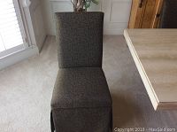 Front view of a dark green dining chair with leaf pattern upholstery and skirted bottom.