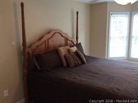 King-size bed with wooden four-poster headboard and mattress dressed in brown checkered bedspread and decorative pillows.