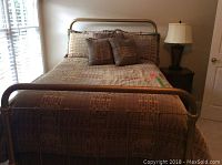 Full view of bed made with brass bed frame, headboard and footboard visible, bedding includes bedspread and pillows