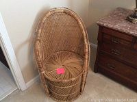 Brown wicker chair with rounded back and circular seat placed next to wooden furniture.