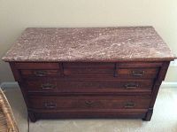 Front view of the brown wood dresser with intact drawers and brown marble top with visible crack.