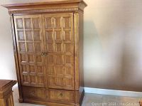 Front view of the closed brown wooden armoire showing paneled double doors, decorative crown molding, and two drawers at the base.