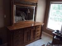 Front angled view of the brown wooden dresser with attached mirror and drawers in a room.