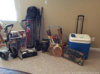 Full view of sporting equipment including Dunlop golf bag with clubs, wooden tennis rackets, tennis display, Everlast boxing gloves, hand weights, and large Igloo cooler