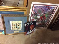 Identifies the lot contents including framed items and book arranged on a floor: Ohio State poster, Atlanta Olympic stamps frame, and Chipper Jones book.