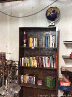 Full view of dark brown wooden bookshelf filled with books, DVDs, and globe on top