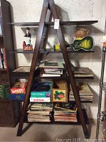 Shelving unit with stacked vinyl records, board games Yahtzee, Guesstures, and wall art signs with laundry theme, small green acoustic guitar, and figurines.