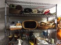 Full view of metal shelving holding tablecloths, napkins, wicker baskets, glassware, and other kitchen items.