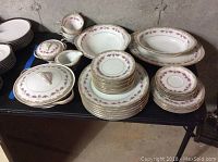 Full overview of Noritake china set arranged on black table. Items include plates, saucers, serving pieces, and covered dishes.