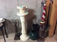 Photo showing ceramic pedestal, fireplace utensils, green vase, candle stick holder, American flag and metal flag holder in a corner.