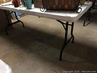 Side view of plastic folding table showing white top and black legs.