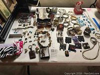 Wide view of multiple pieces of costume jewelry, watches, earrings, bracelets, rings, and sunglasses spread on a table.