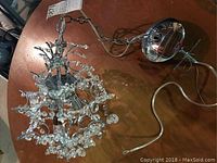 Full view of glass chandelier laid on a wooden table showing glass pendants and silver metal canopy with wiring.