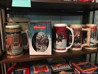 Nine Budweiser Christmas beer steins on a shelf with three Budweiser branded boxes - boxes empty, may not match steins.