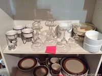 Photo showing 6 clear wine glasses, 4 white bowls with black stripes, 3 McCoy nesting bowls, 4 small white heating bowls with candle holders, and brown dishes including plates, saucers, salad plates, and coffee cups.