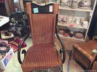 Front angle of the wood and wicker rocking chair showing seat, backrest, and metal arms.