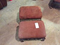 Two brown cloth foot stools on concrete floor, viewed from above showing the padded rectangular tops and iron legs.