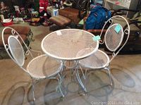 Full view of white iron round patio table with two matching chairs on concrete floor, showing rust on table surface.