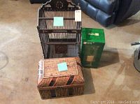 Photo showing the metal bird cage, rectangular wicker chest, and JC Penney hurricane candle holder in box arranged on floor.