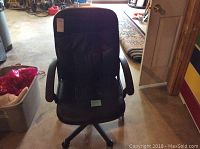 Black office chair with cushioned seat, armrests, and wheels in a garage setting