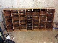 Full front view of the wooden mail sorting shelf with many individual cubby-like compartments for sorting mail or documents. Shelf stands against a concrete wall.
