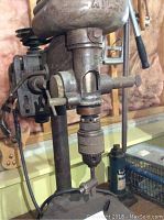 Close-up photo of the upper section of the Atlas drill press showing the chuck, column, and part of the motor housing labeled 'Atlas'.