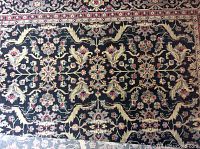 Top view of the Harold area rug showing the main field with floral and leaf patterns in black, gold, gray, and reds.