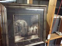 Framed print with urban night archway scene and dim street lamps in sepia tones, large square frame with wide silver border.