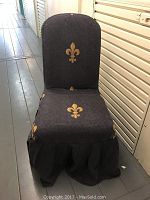 Front view of dining chair showing black cover with gold fleur de lis pattern and ruffled skirt base.
