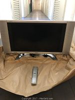 Front view of Sharp Aquos flat screen TV on a silver stand with a remote in front.