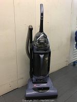 Hoover upright vacuum cleaner standing with hose attached on side.