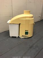 Side view of yellow Juiceman Jr. juicer with attached refuse container, showing overall shape and refuse container condition.