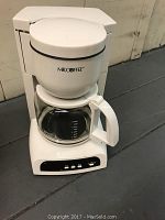 Front view of white Mr. Coffee drip coffee maker with glass carafe containing coffee inside and filter basket on top