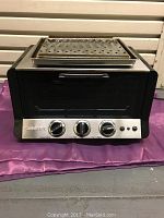 Front view of the Cuisinart toaster oven showing stainless steel control panel with three knobs and removable perforated tray on top.